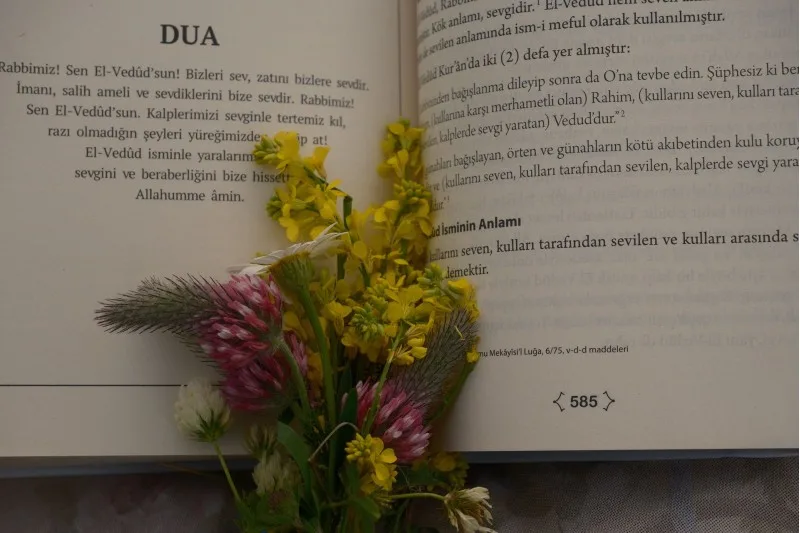 Türkçe dua metni bulunan açık kitap ve kır çiçekleri