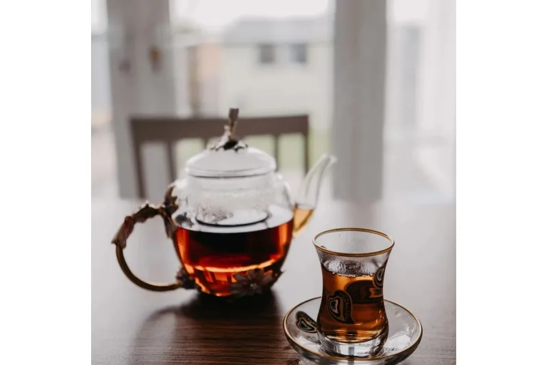 Ahşap masada cam demlik ve tabaklı ince belli çay bardağı